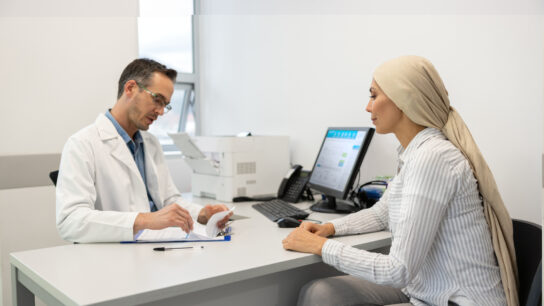 Oncologist talking to a female patient wearing a headscarf during a consultation at his office.