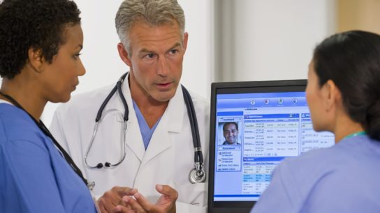 Clinicians talking with an electronic health record showing on the screen