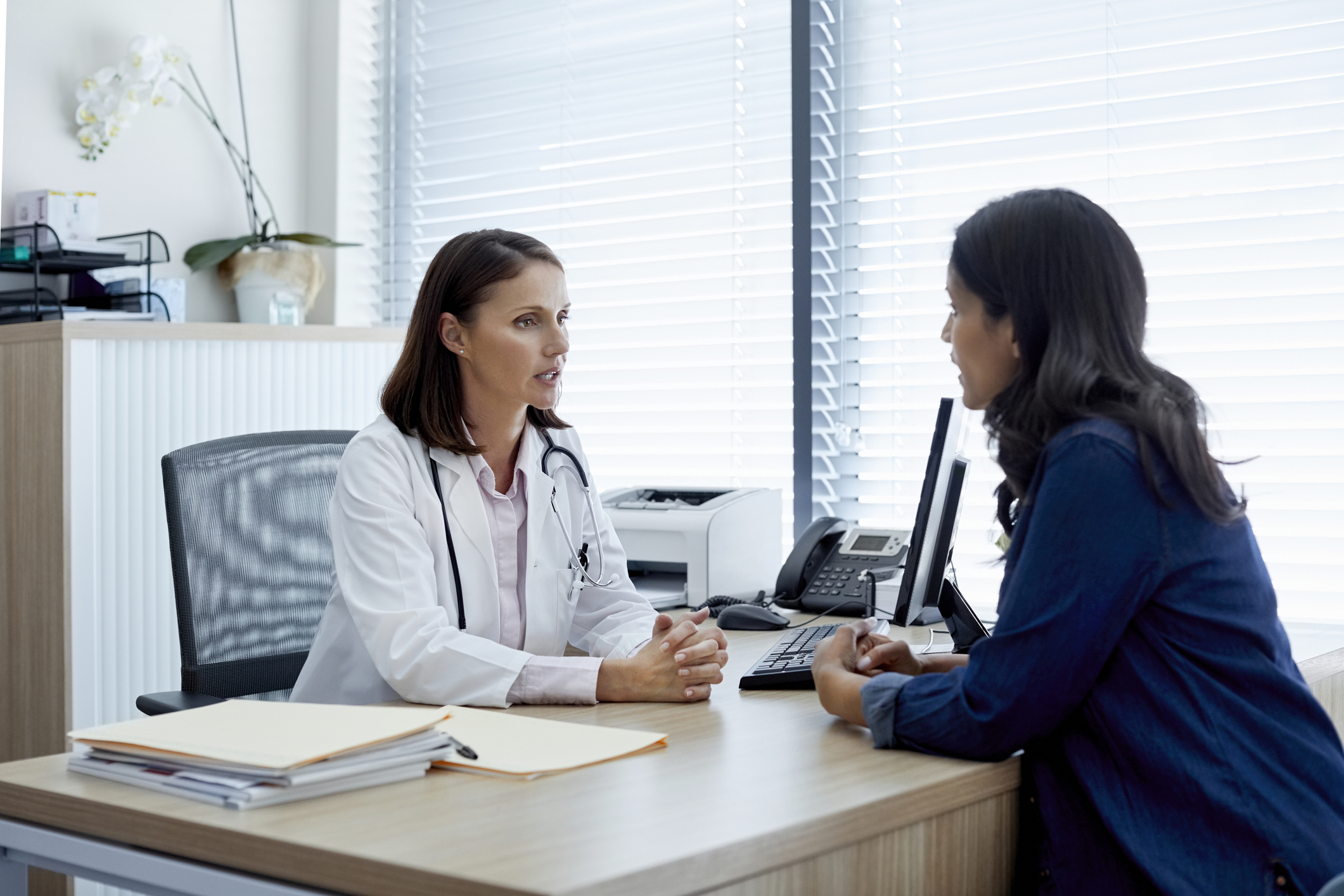 Doctor talking with female patient at desk.