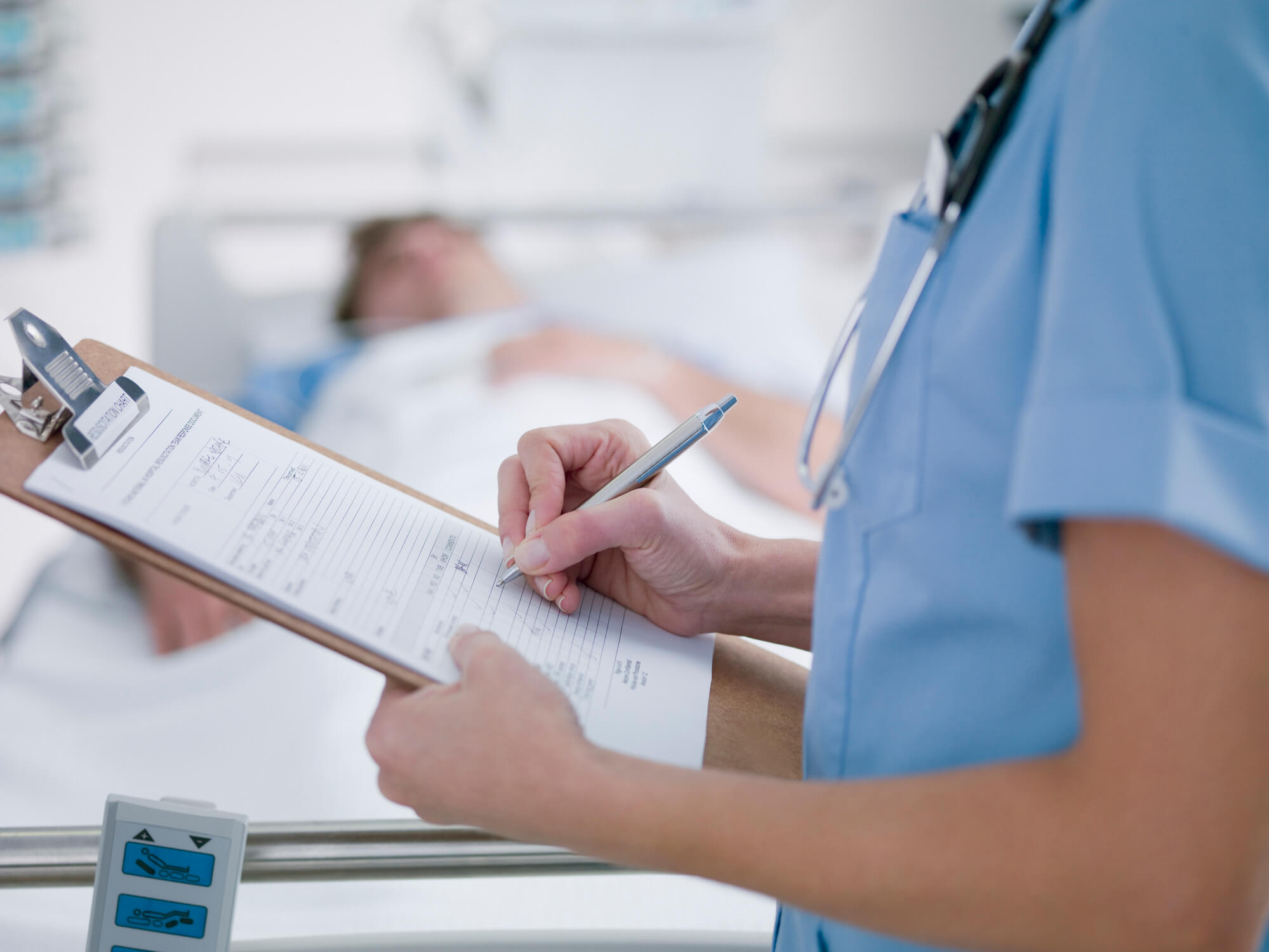 Nurse writing in chart beside patient in hospital bed.