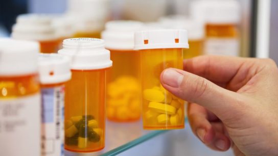 A woman reaching for a prescription bottle in a medicine cabinet