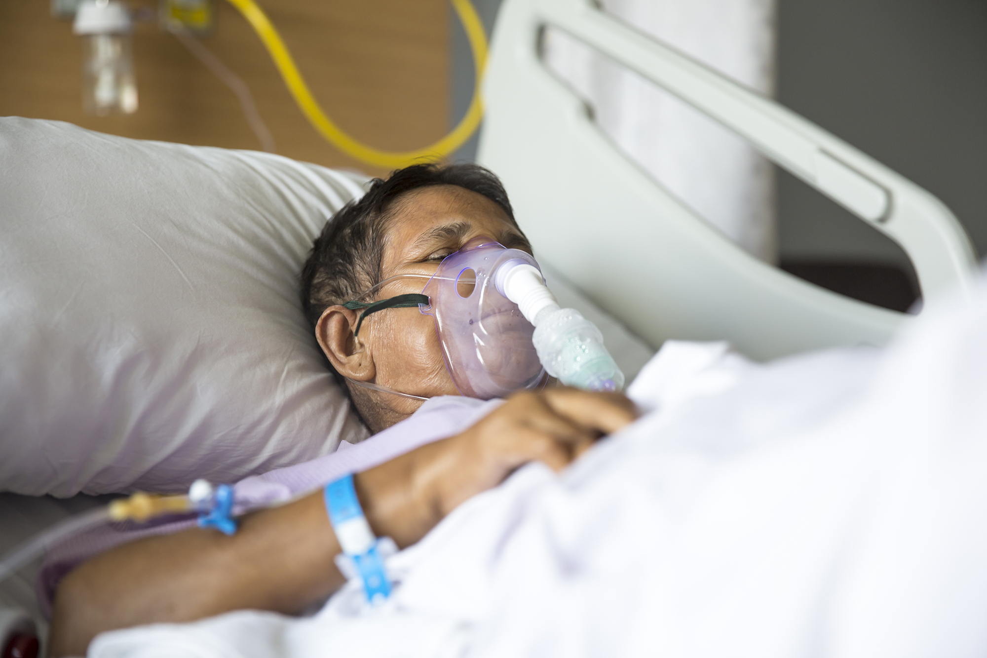 Patient lying on Hospital bed with ventilator mask on her nose.